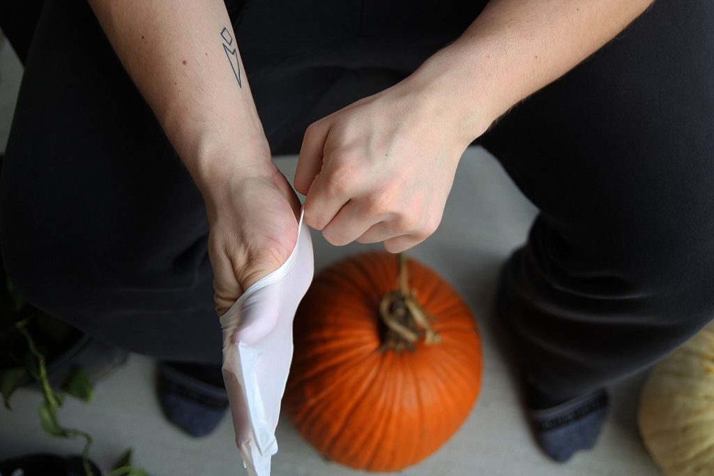 gloved hands with a pumpkin on the floor