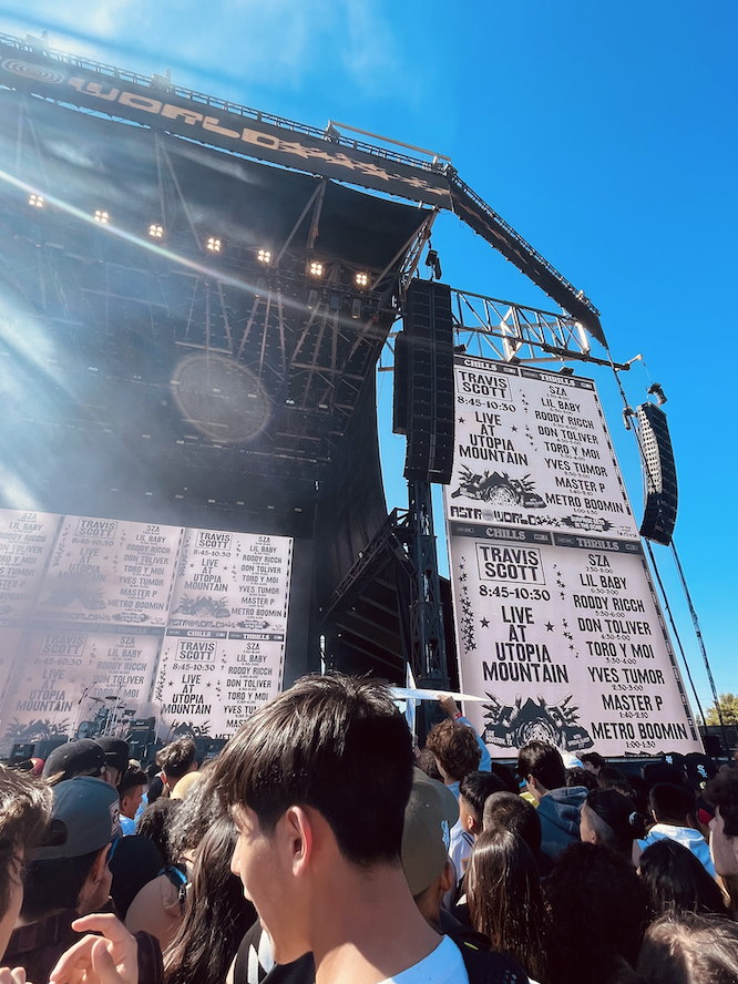Many people in a crowd in front of a massive outdoor stage at the Astroworld Festival. Screens display the schedule for day-one with Travis Scott headlining.
