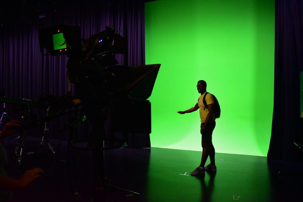 A man stands in front of a green screen while he talks about the weather. 