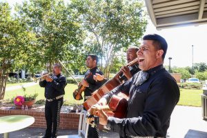 Four mariachi members playing instruments including guitars, a violin, a trumpet, and singing are performing in the South Austin Campus courtyard