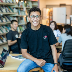 Asian male student in library smiling at camera.
