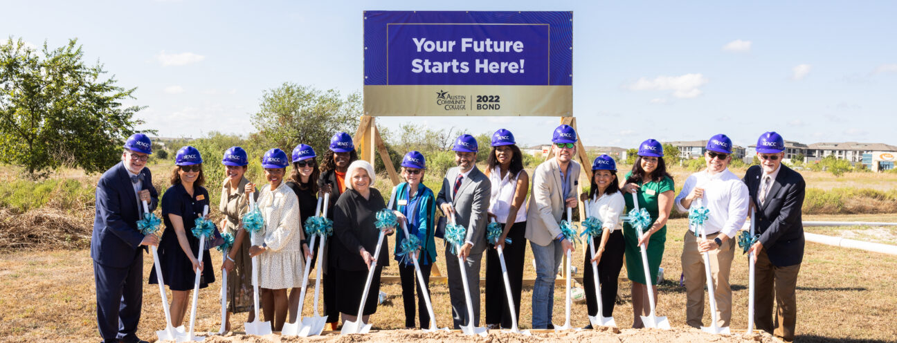 A group of diverse individuals stands in front of a large sign that reads "Your Future Starts Here!" They are gathered around a wooden platform filled with sand, each holding a shovel. Everyone is wearing blue hard hats and teal ribbons, symbolizing a groundbreaking ceremony. The background features a clear blue sky and some greenery.