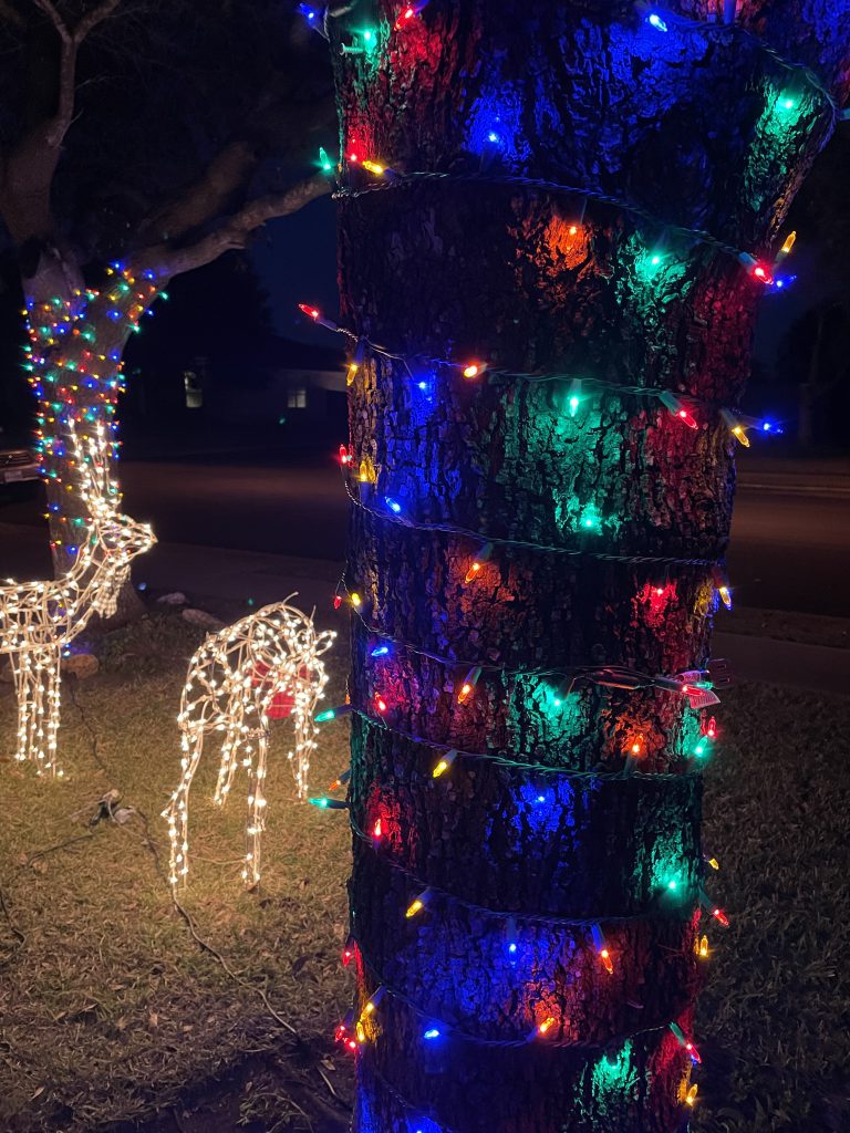 close up of a tree wrapped in LED lights next to two light up reindeer  