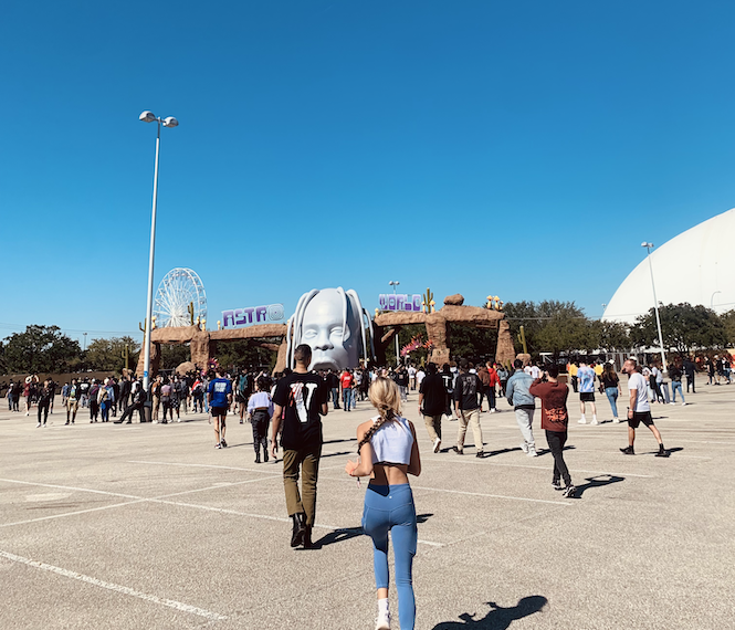 People flock towards the entrance of the Astroworld Festival. It is a bright, cloudless day and many young people walk and run in the direction of a huge inflatable Travis Scott head.
