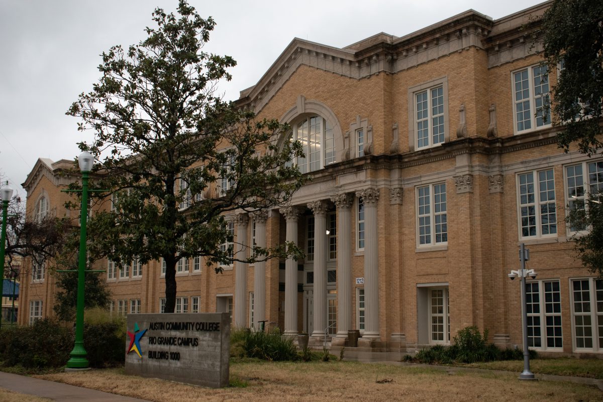 A three-story building with roman columns at the entrance and masonry details from the early 20th century is the main focus of the photo. In front of the building is a cement sign that reads "Austin Community College Rio Grande Campus Building 1000."