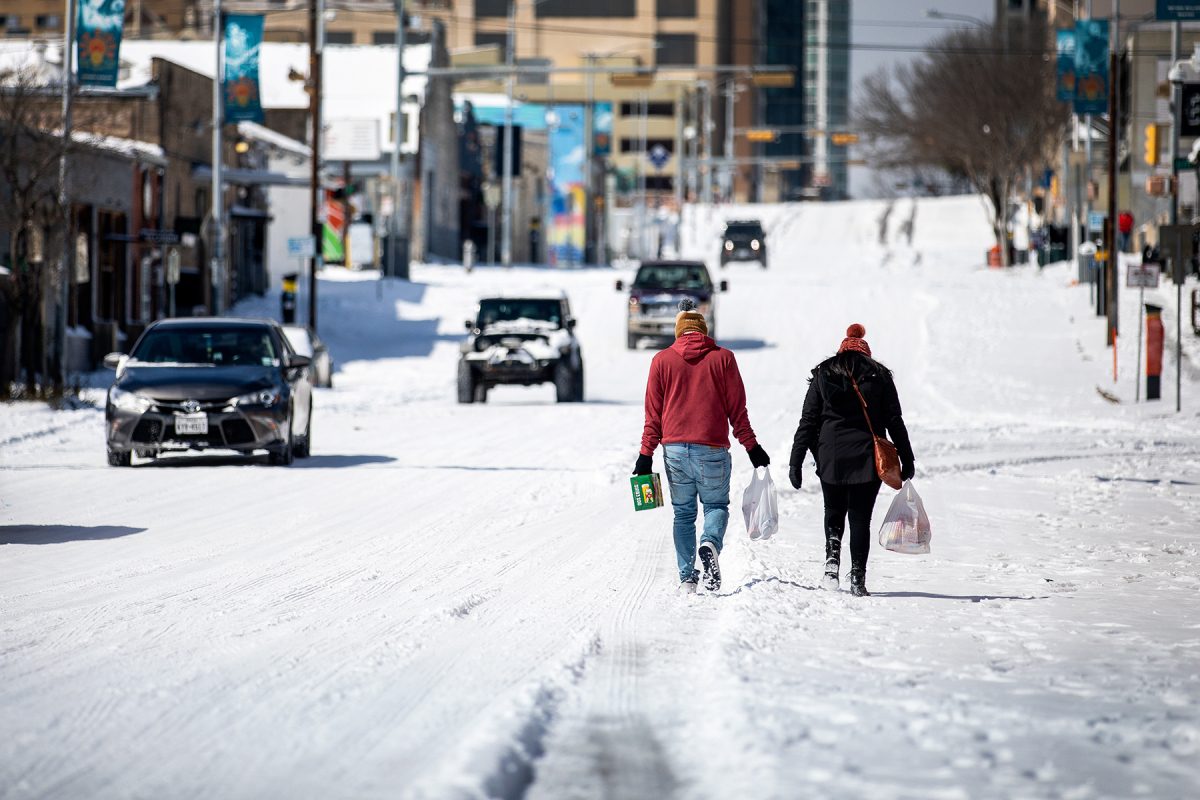 Two people walk in a snow covered road with groceries in Austin during February 2021's winter storm.