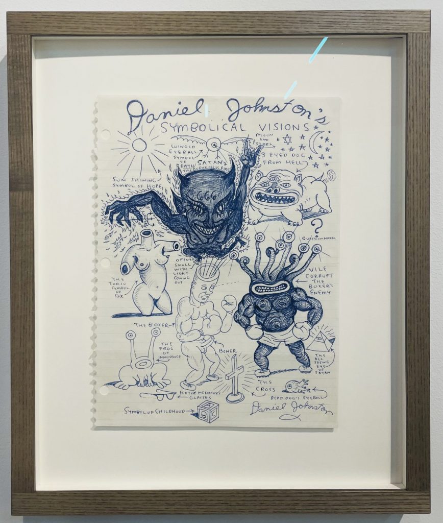 Wild images from Daniel Johnston portray a sinister looking devil, a three-eyed dog from hell, a boxer with an erection fighting a many eyed monster are some of the many images drawn.