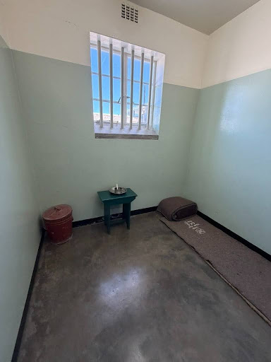 Nelson Mandela’s former prison cell on Robben Island, showing the cramped 7-by-9-foot quarters and minimal bedding where he spent 18 years of his imprisonment.
