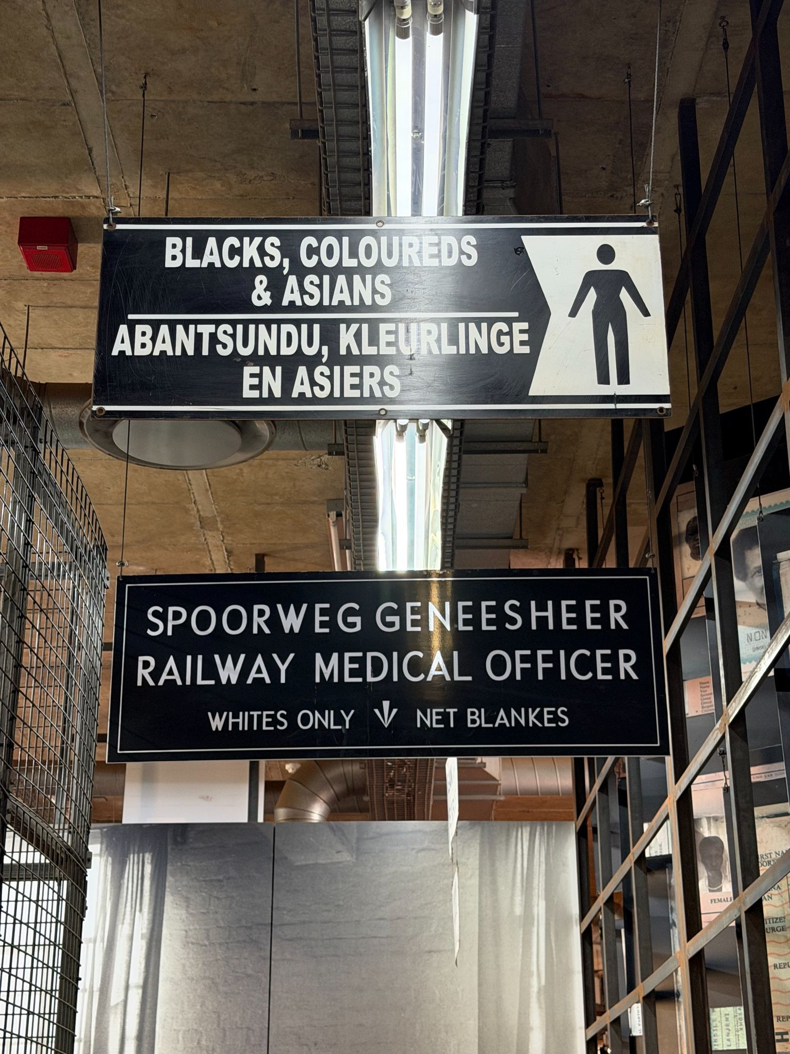 Historical apartheid-era sign written in English and Afrikaans outlining racial segregation rules for passengers at a railway station