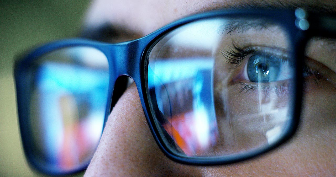 Closeup of man's glasses reflecting computer screens