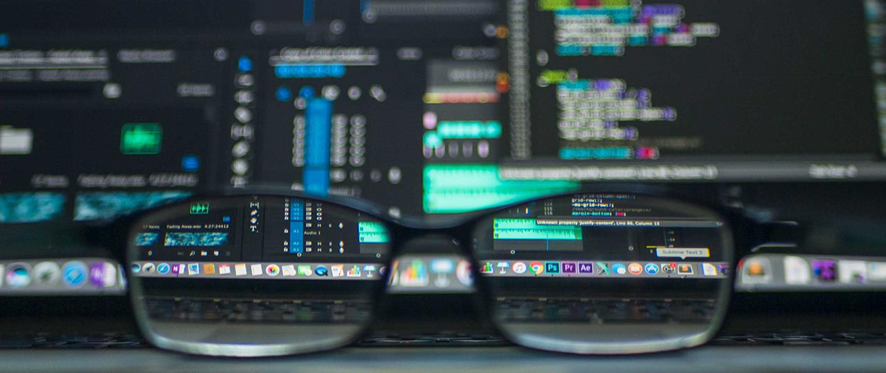 A pair of glasses in front of a computer screen filled with code.