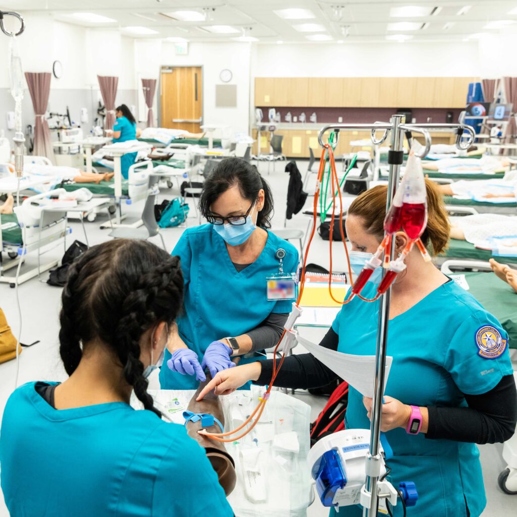 Austin Community College nursing students in blue scrubs practice intravenous therapy together in a clinical skills lab.