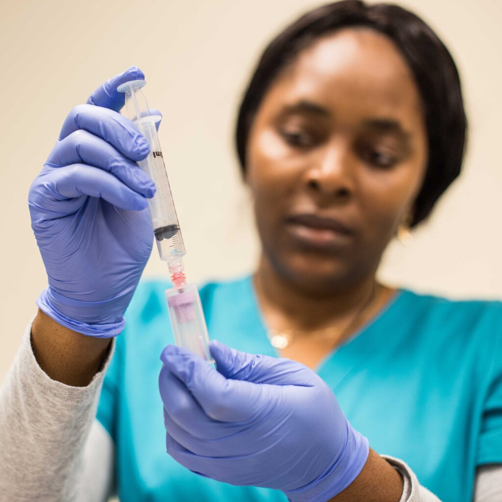 Austin Community College Health Sciences student wearing blue scrubs and gloves draws liquid into a syringe during clinical skills training.