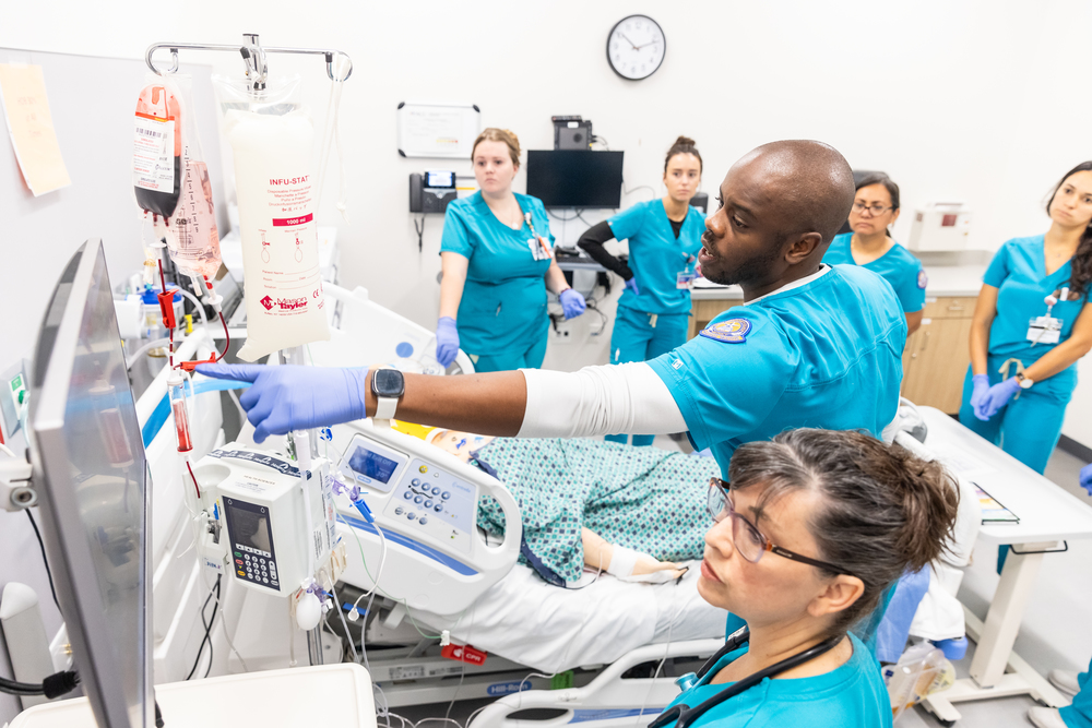 Professional Nursing students training during class with monitors and hospital bed