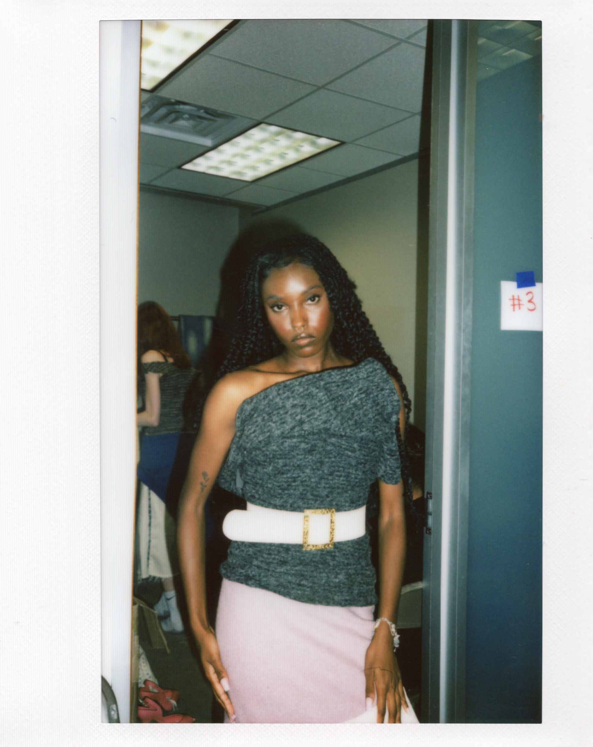 Woman poses in grey top and pink skirt in front of the camera before Fashion Show