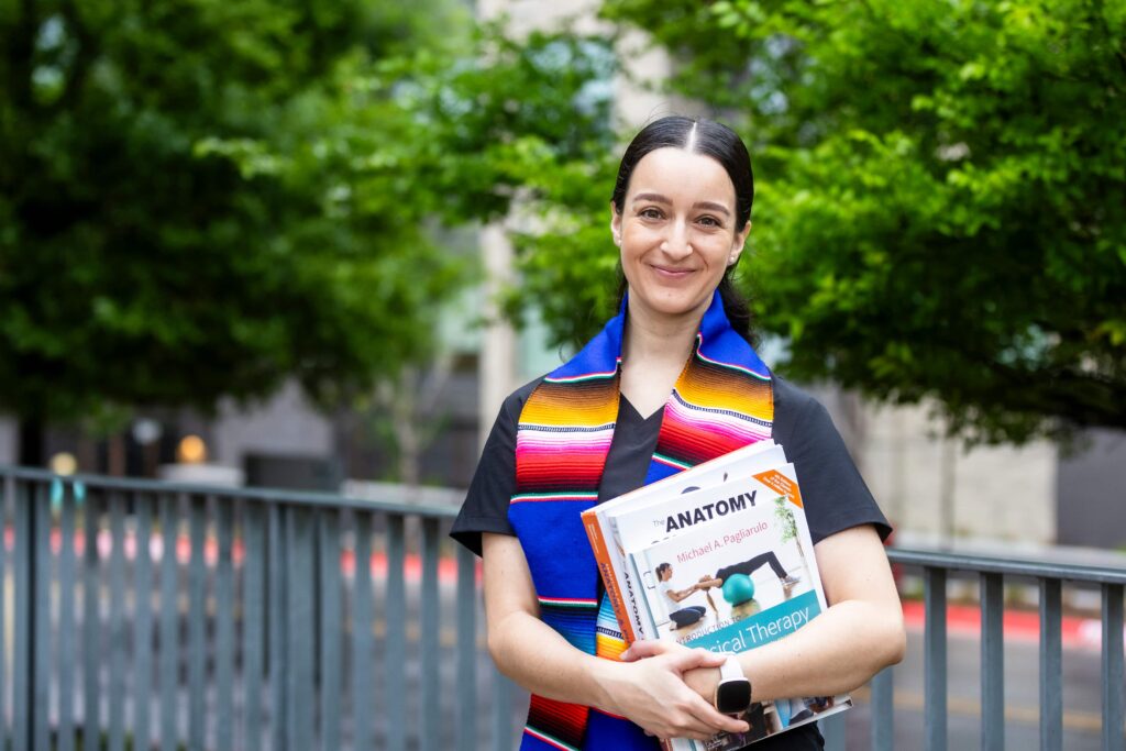 Photo of student holding textbooks while smiling at the camera