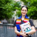 Photo of student holding textbooks while smiling at the camera