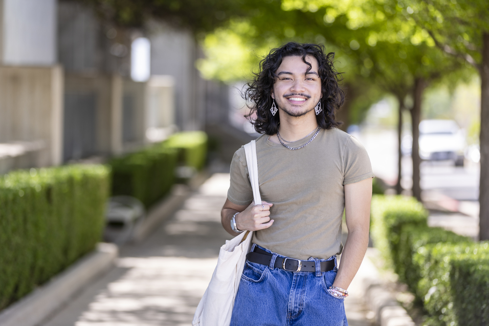 Student smiles at the camera with trees behind him