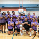 Group of volleyball players posing on a court with the riverbat sign