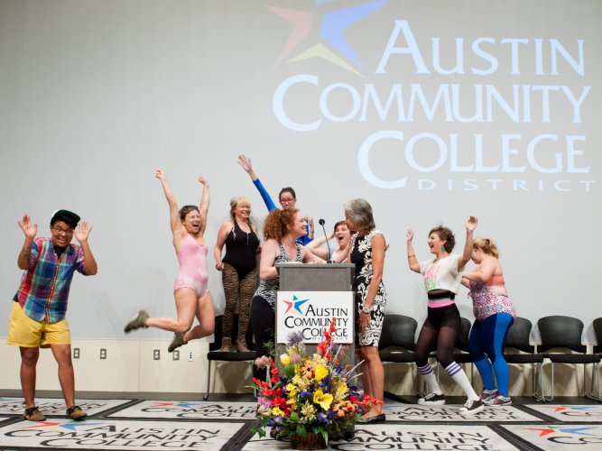 Individuals in exercise gear jump and celebrate behind Erica Nix at podium receiving recognition