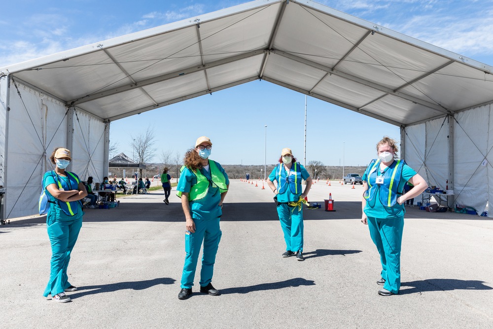 Four student volunteers wearing scrubs and masks at vaccination clinic at Circuit of the Americas