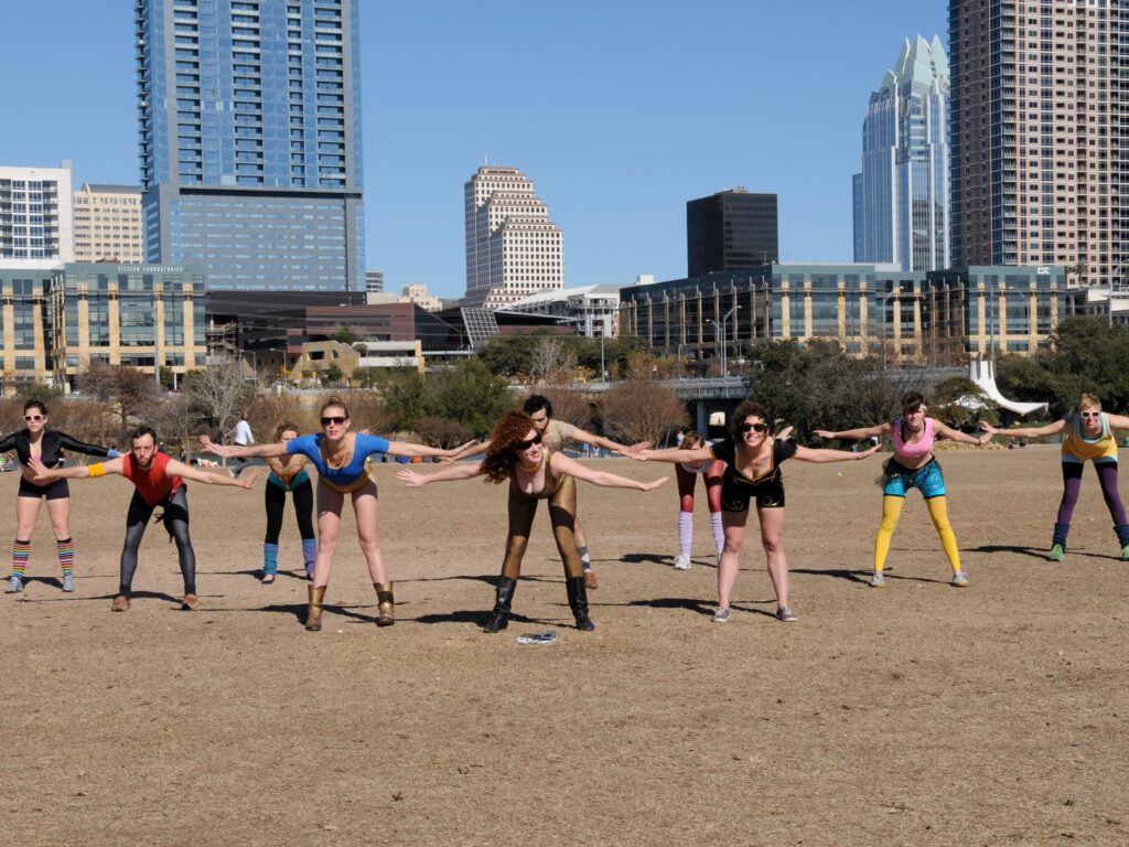 Group of males and females in colorful exercise clothing working out at Town Lake with Austin skyline behind
