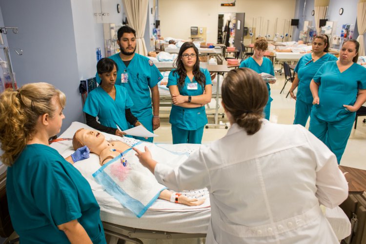 Instructor instructs male and female students working with simulation dummy in nursing lab