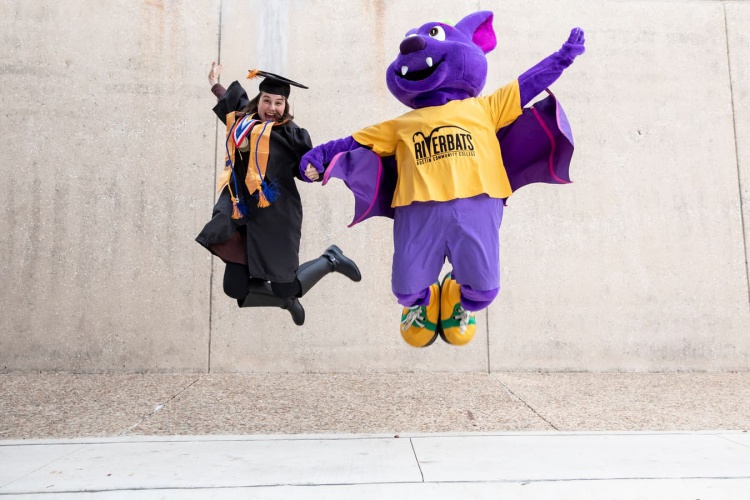 Jamille Souza Madeira and mascot R.B. jump in the air in celebration outside building at 2019 commencement 