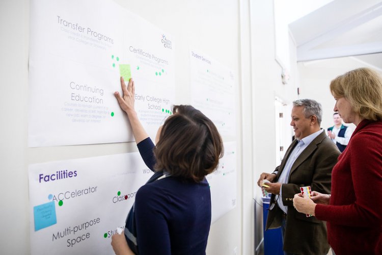 Two females and one male participate in brainstorming exercise applying colorful stickers and notes to wall posters 