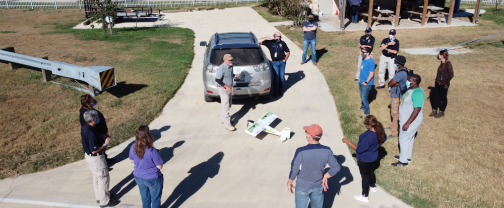 Individuals gather around instructor demonstrating drone airplane