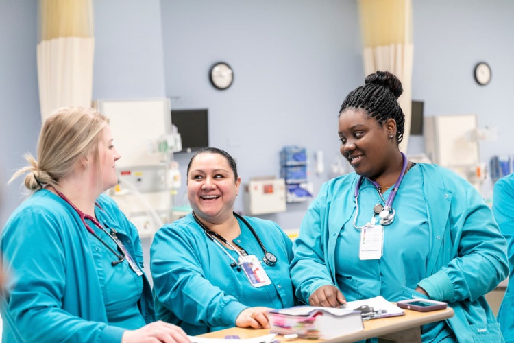 Three smiling female nursing students wearing scrubs in simulation lab