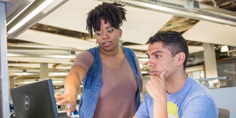 Male student views computer monitor while female student coach points to monitor