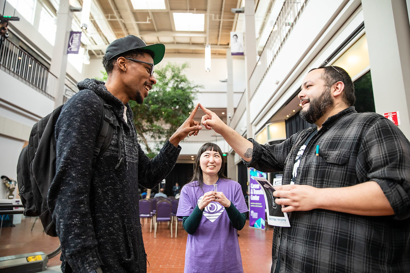 Two diverse males face each other while touching index fingers with female looking on