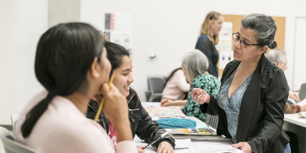 Instructor converses with two female Latino students