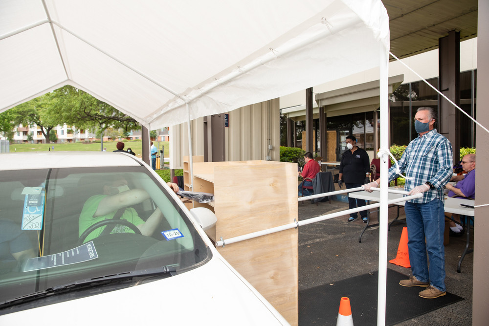 ACC President Dr. Richard Rhodes gives a wrapped laptop computer to a male student in a car through a drive-thru distribution system
