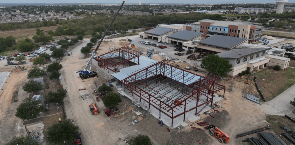 Photo from the air of the shell of a building. There is construction equipment and the beams are up