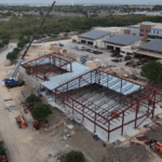 Photo from the air of the shell of a building. There is construction equipment and the beams are up