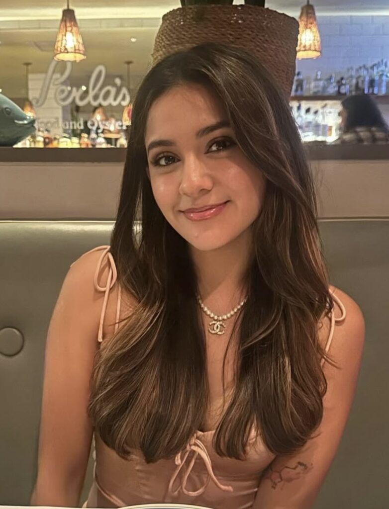 photo of student with brown hair and pink tank top, smiling at the camera sitting in a booth at a restaurant